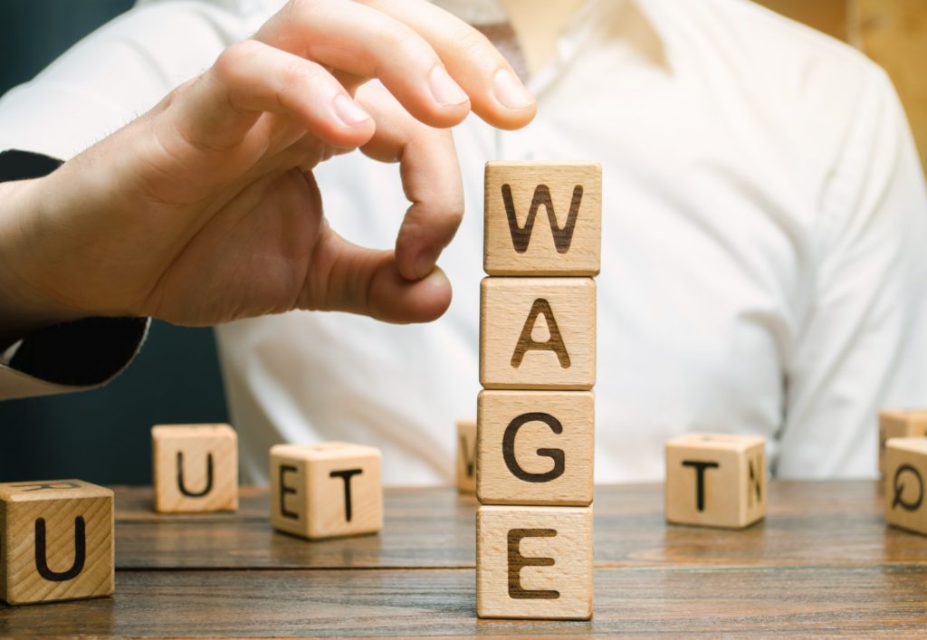 Hand of a businessman removes wooden blocks with the word Wage